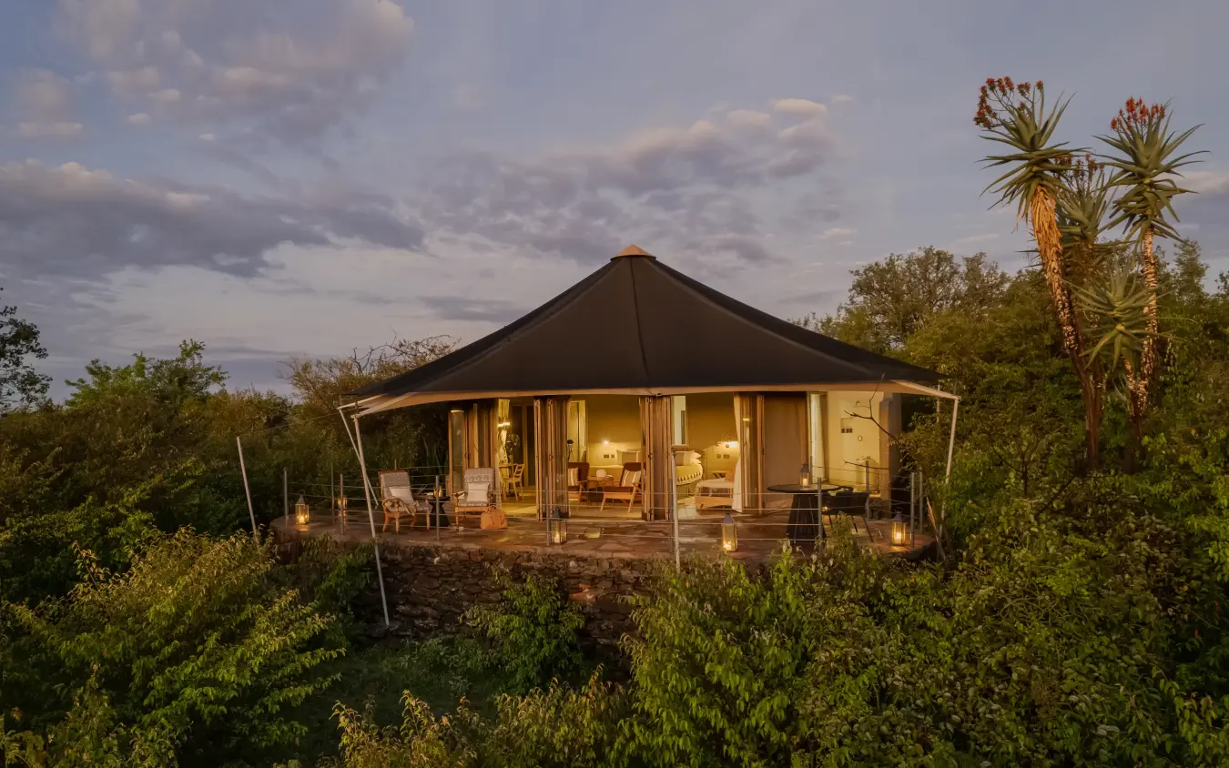 Luxury safari tent with illuminated interior at dusk surrounded by bush vegetation, Hemingways Ol Seki Mara, Maasai Mara, Kenya