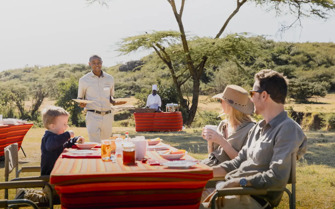 Family enjoying outdoor dining under acacia trees in savanna landscape, Hemingways Ol Seki Mara, Maasai Mara, Kenya