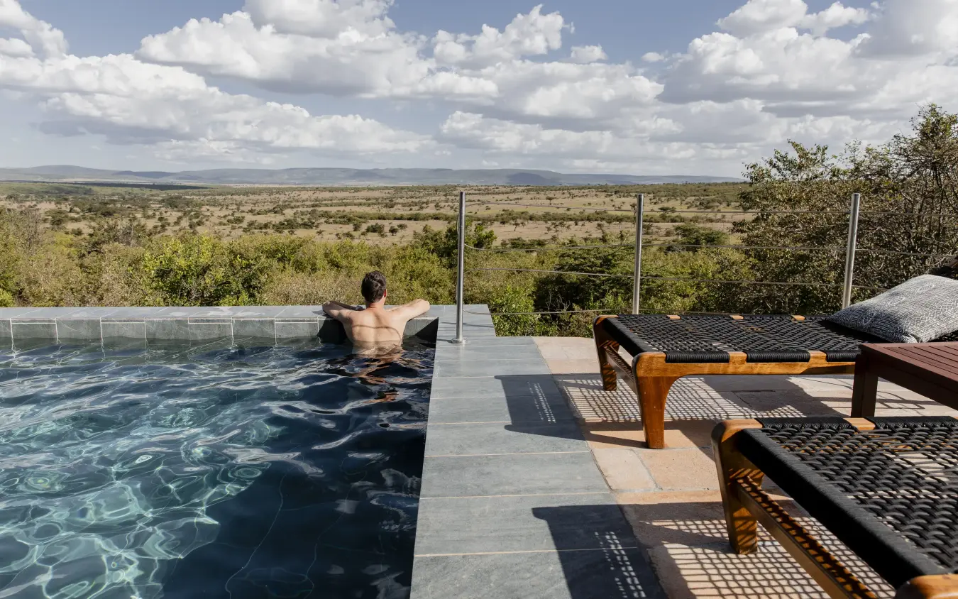 Guest relaxing in infinity pool overlooking vast savanna landscape, Hemingways Ol Seki Mara, Maasai Mara, Kenya