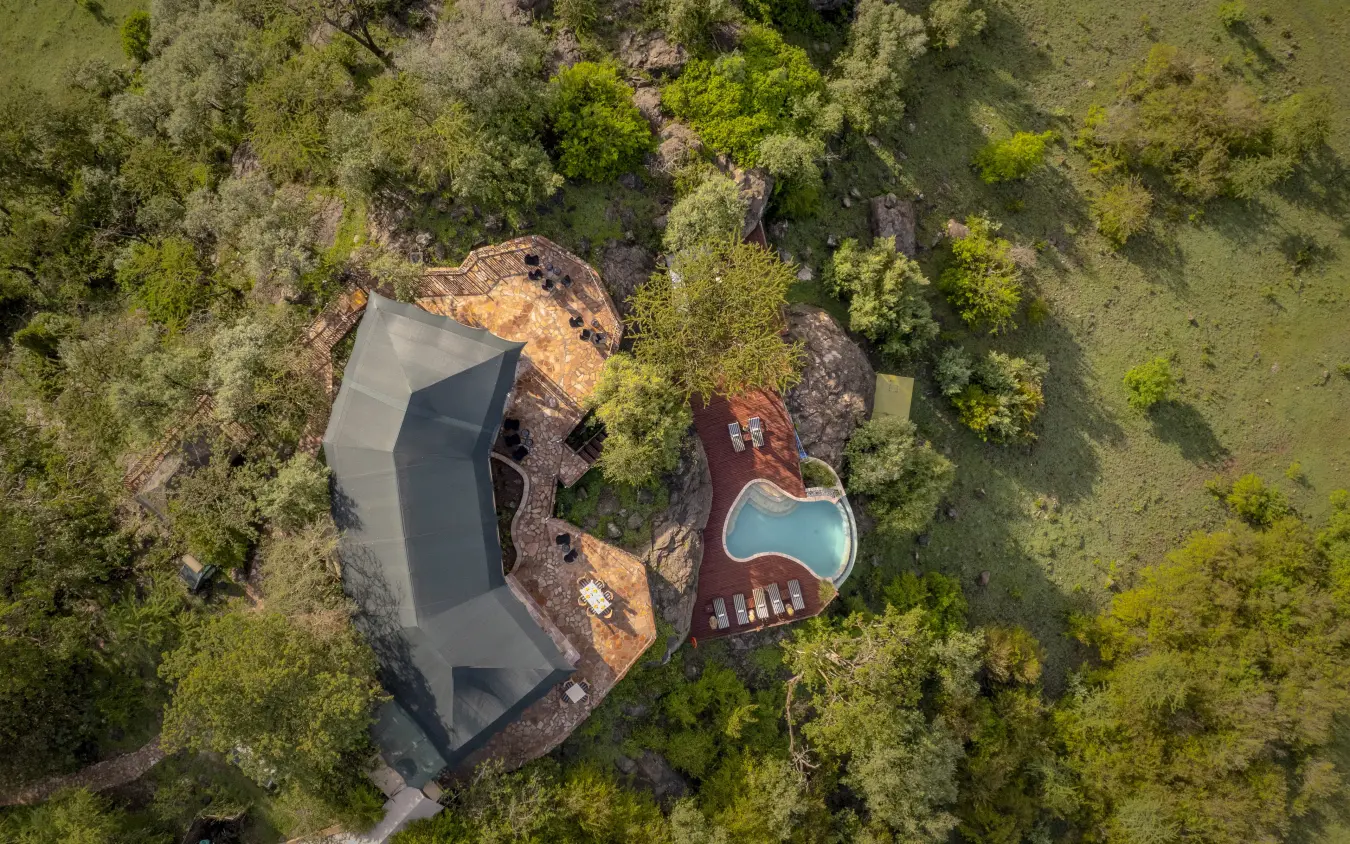Luxury lodge with dark roof nestled among dense forest trees and pool, Hemingways Ol Seki Mara, Maasai Mara, Kenya