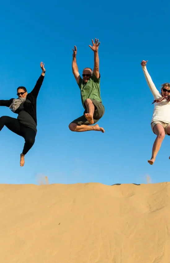 Three people jumping on sand dune against blue sky, Hoanib Skeleton Coast Camp, Skeleton Coast, Namibia