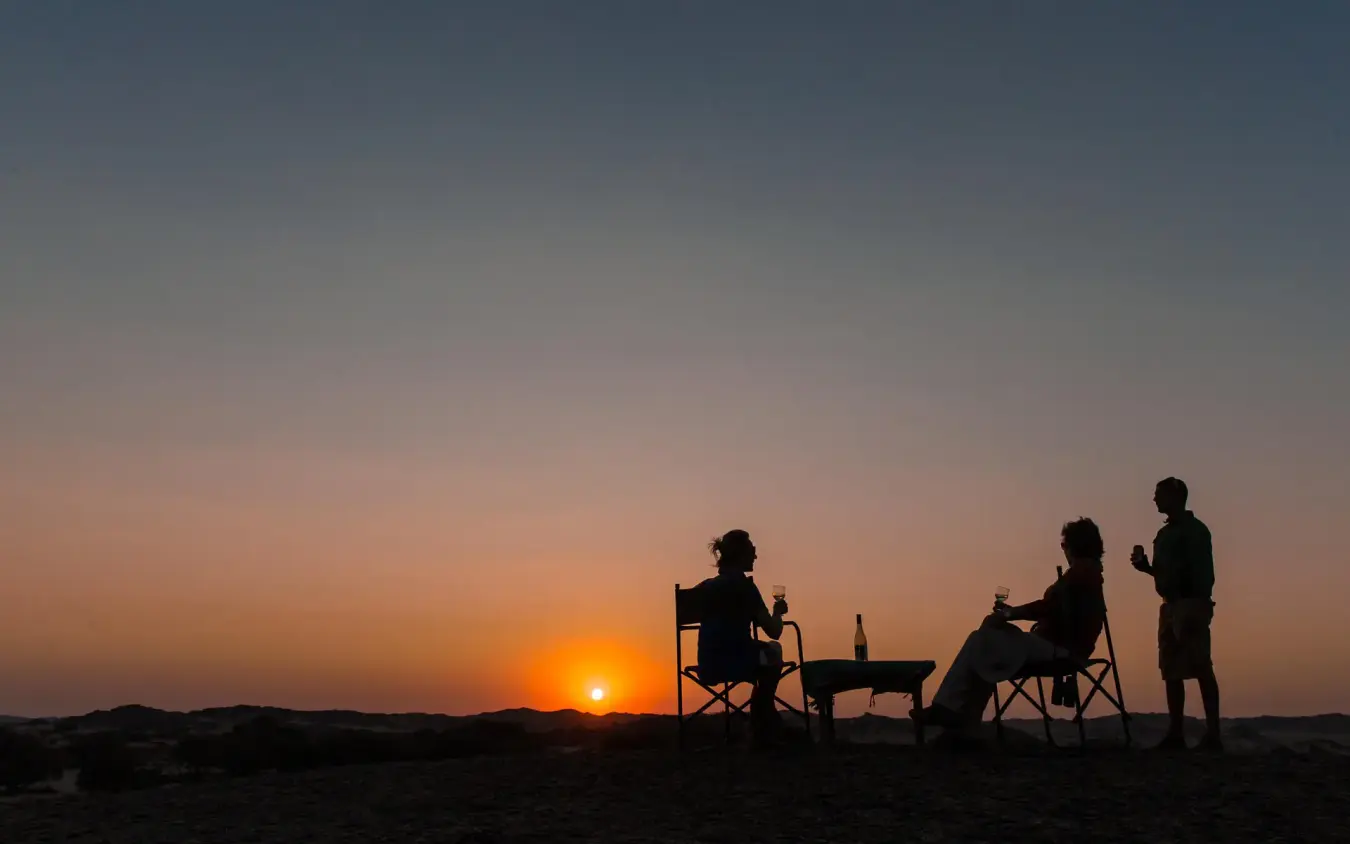 Group enjoying sunset drinks on desert beach, Hoanib Skeleton Coast Camp, Skeleton Coast, Namibia