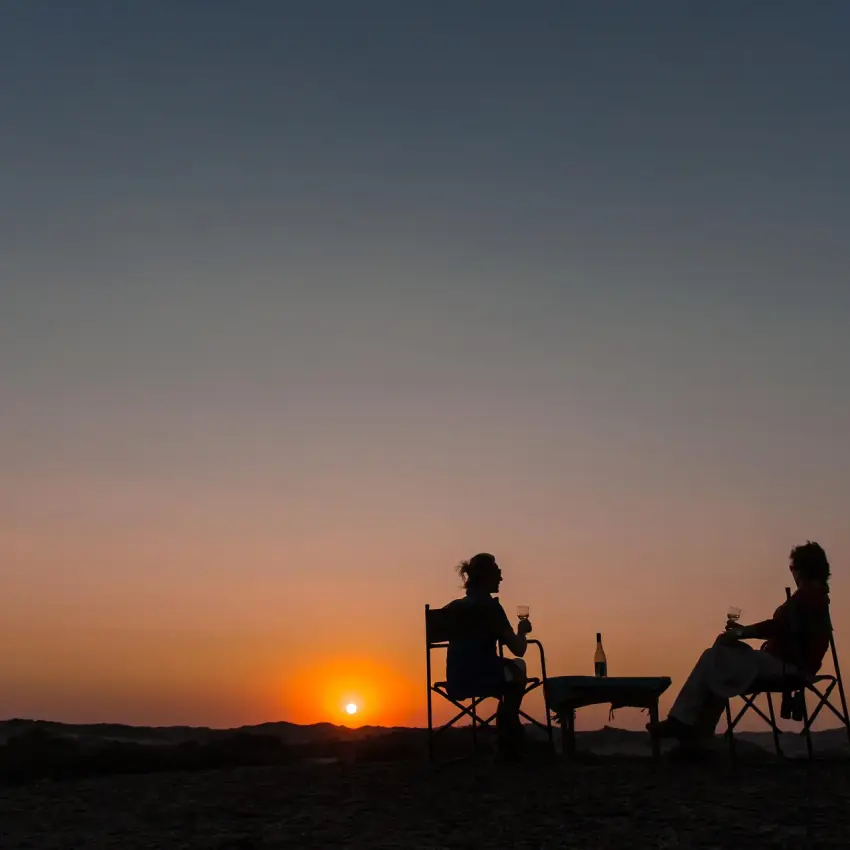 Group enjoying sunset drinks on desert beach, Hoanib Skeleton Coast Camp, Skeleton Coast, Namibia