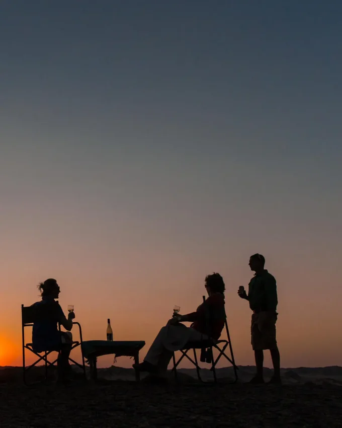 Group enjoying sunset drinks on desert beach, Skeleton Coast, Namibia