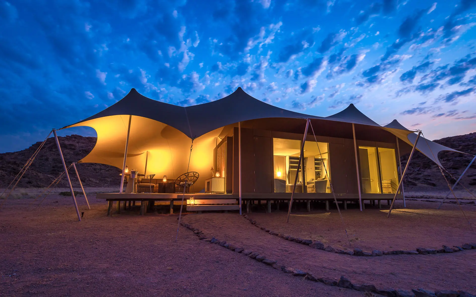 Illuminated luxury tent camp at dusk in desert landscape, Hoanib Skeleton Coast Camp, Skeleton Coast, Namibia