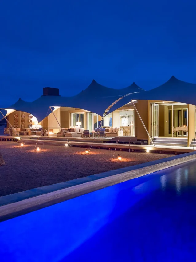 Illuminated pool with tent accommodations and desert landscape at dusk, Hoanib Skeleton Coast Camp, Skeleton Coast, Namibia