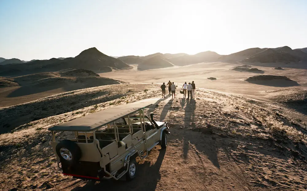Safari vehicle with group overlooking vast desert valley landscape, Hoanib Valley Camp, Damaraland, Namibia