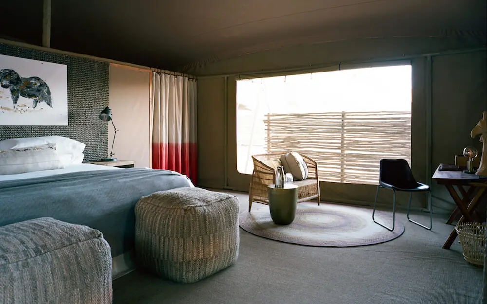 Spacious bedroom with bed, seating area, and glass doors, Hoanib Valley Camp, Damaraland, Namibia
