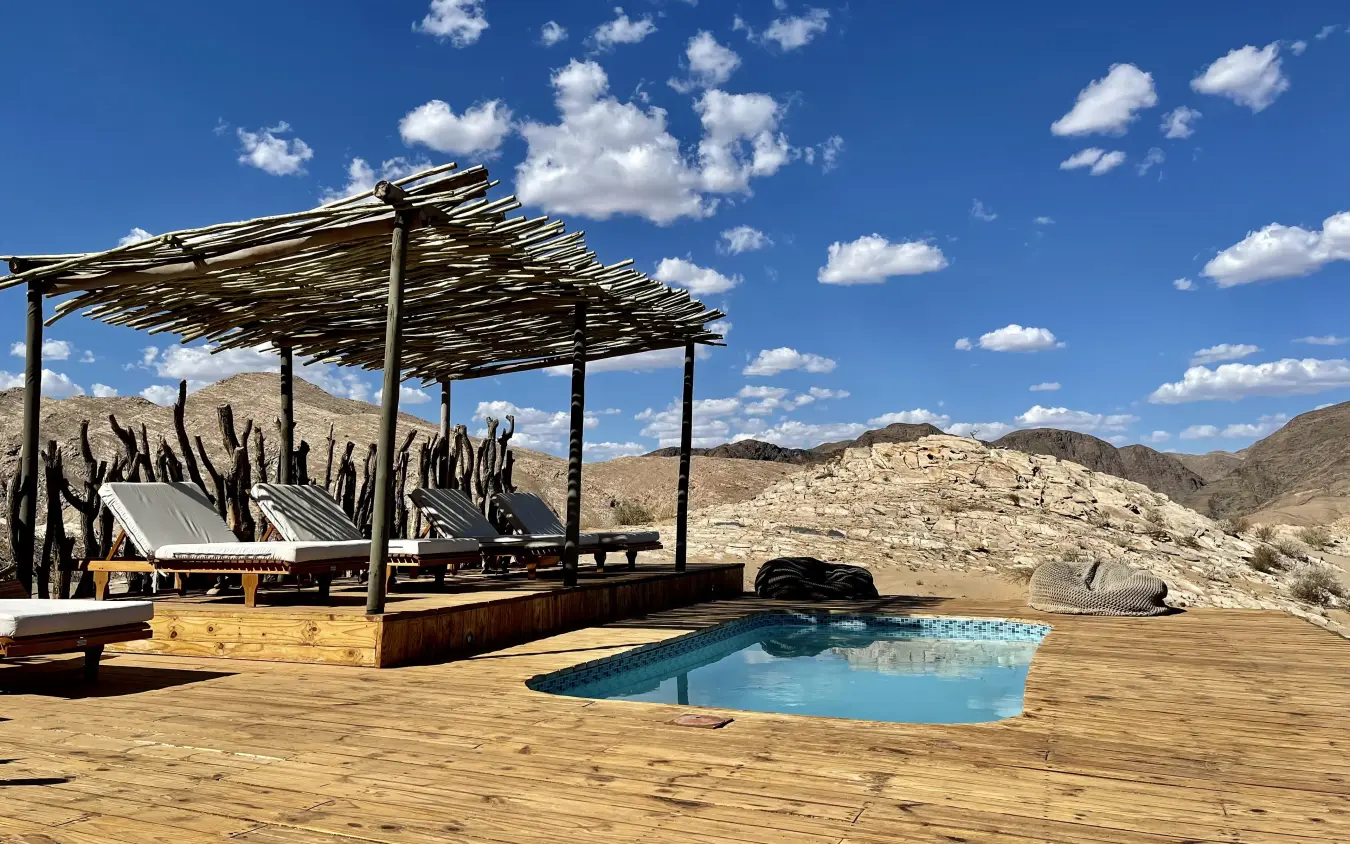 Desert lodge pool area with lounge seating and mountain views, Hoanib Valley Camp, Damaraland, Namibia