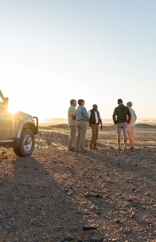 Group of guests gathered near safari vehicle in desert landscape, Sossusvlei, Namibia