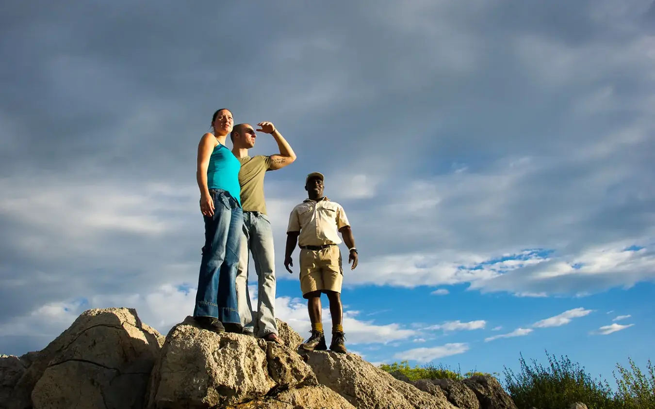 Three hikers standing on rocky outcrop against cloudy sky, Horizon by Ongava, Etosha National Park, Namibia