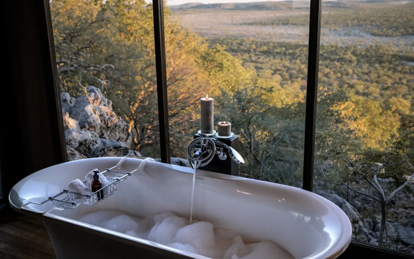 Freestanding bathtub filled with water overlooking forested valley landscape, Horizon by Ongava, Etosha National Park, Namibia