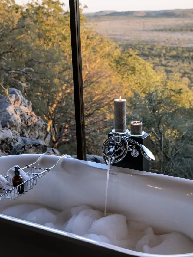 Freestanding bathtub filled with water overlooking forested valley landscape, Horizon by Ongava, Etosha National Park, Namibia