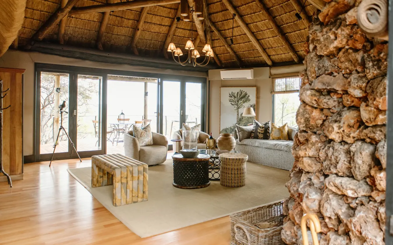 Thatched-roof lounge with stone fireplace and expansive glass doors overlooking bush, Horizon by Ongava, Etosha National Park, Namibia