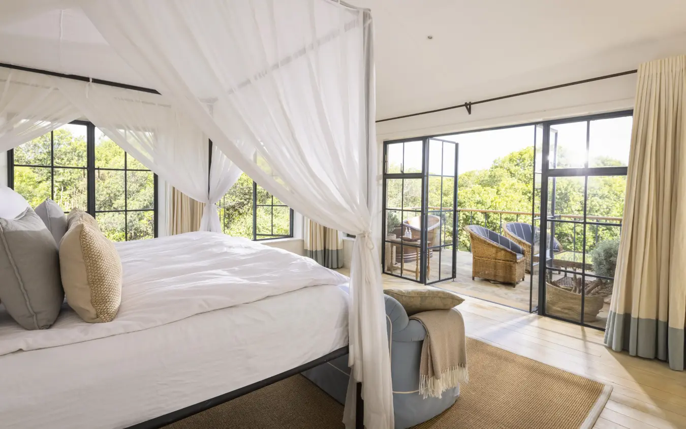 Canopy bed in bright bedroom with large windows overlooking landscape, House In The Wild, Maasai Mara, Kenya