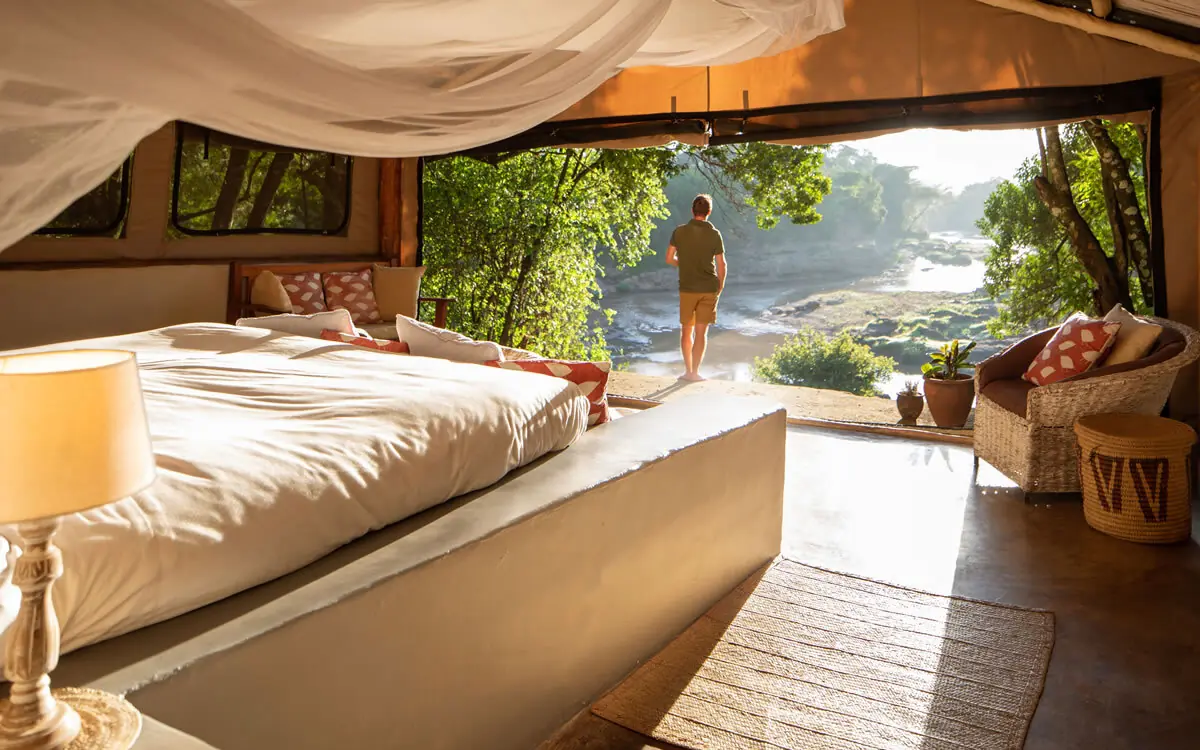 Bedroom with open doors overlooking river and trees, House In The Wild, Maasai Mara, Kenya