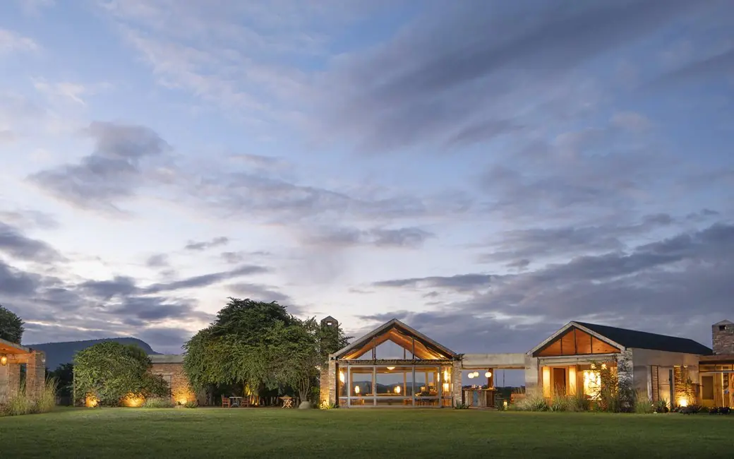 Illuminated lodge buildings at dusk with manicured lawns, House In The Wild, Maasai Mara, Kenya