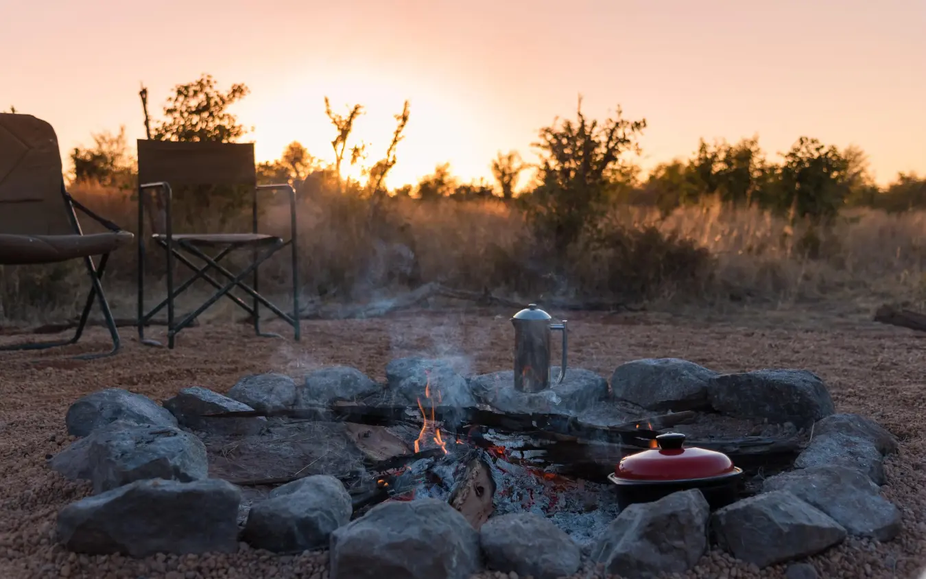 Campfire setup at sunset with camping chairs and cooking equipment, Hwange Bush Camp, Hwange National Park, Zimbabwe