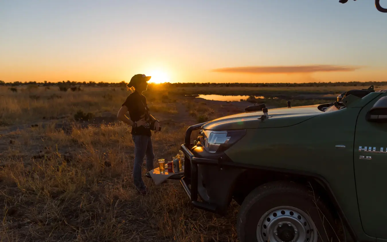 Guide standing by safari vehicle at sunset overlooking waterhole, Hwange Bush Camp, Hwange National Park, Zimbabwe