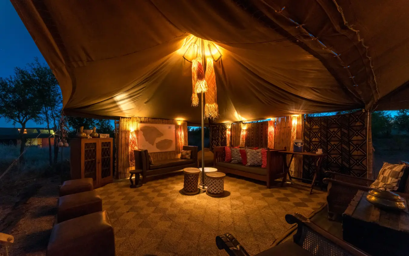 Illuminated canvas tent lounge with seating around central fire, Hwange Bush Camp, Hwange National Park, Zimbabwe