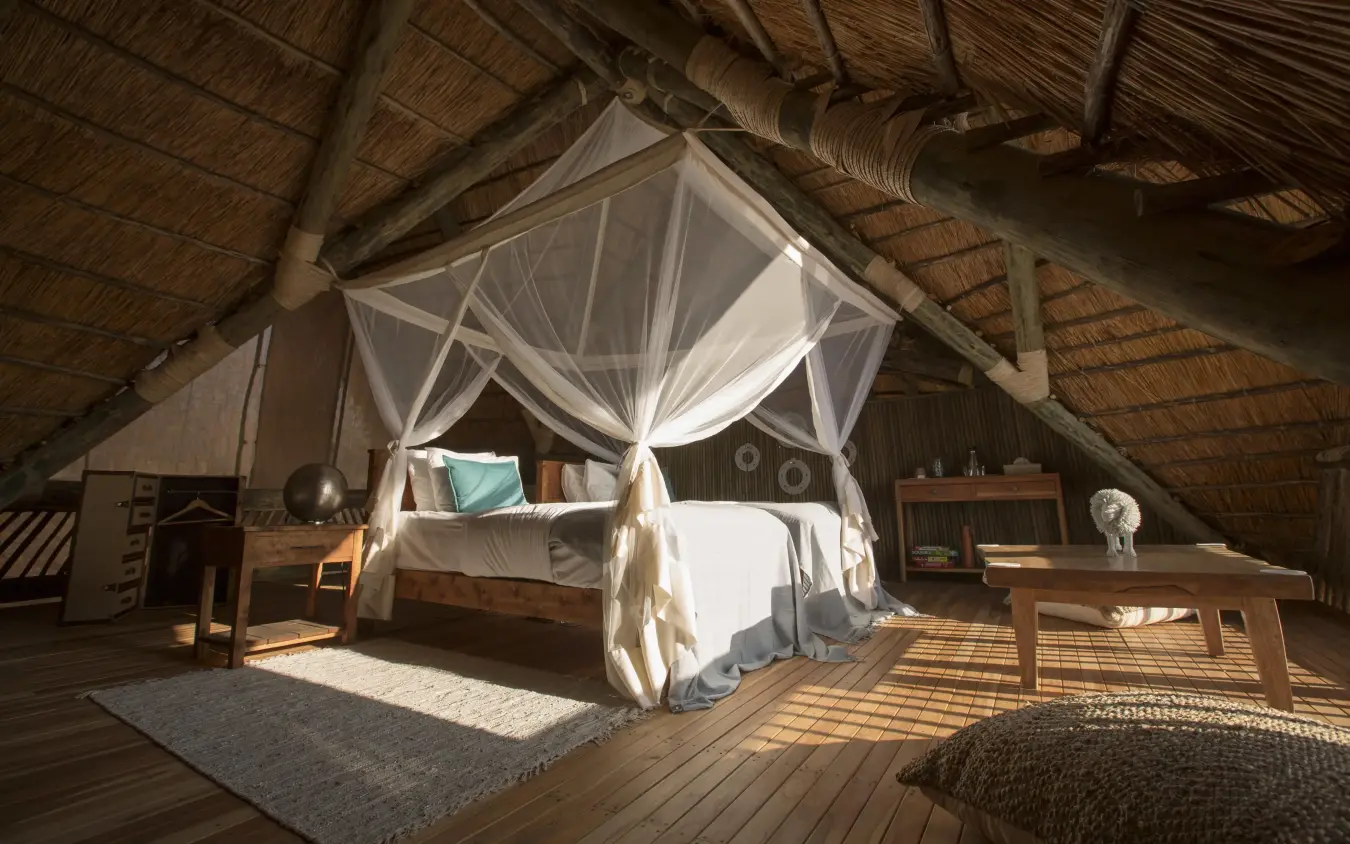 Spacious bedroom with four-poster bed and thatch roof, Ikuka Safari Camp, Ruaha National Park, Tanzania