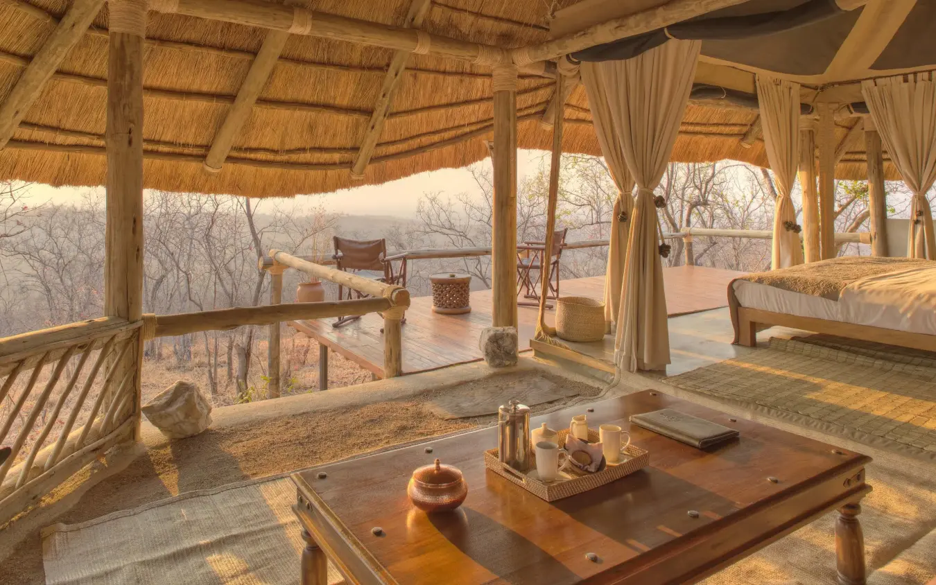 Open-air lounge with wooden furniture overlooking savanna landscape, Ikuka Safari Camp, Ruaha National Park, Tanzania