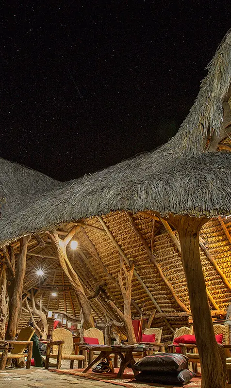Illuminated thatched-roof lodge structure at night with wooden interior, Il Ngwesi, Laikipia Highlands, Kenya