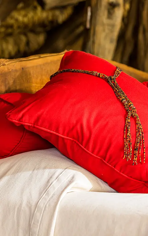 Red pillows with gold tassels on wooden bed frame, Il Ngwesi, Laikipia Highlands, Kenya