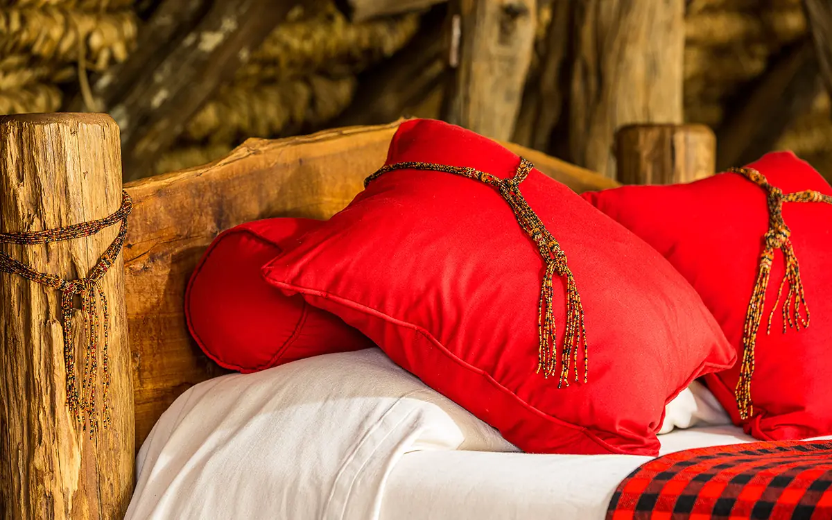 Red pillows with gold tassels on wooden bed frame, Il Ngwesi, Laikipia Highlands, Kenya