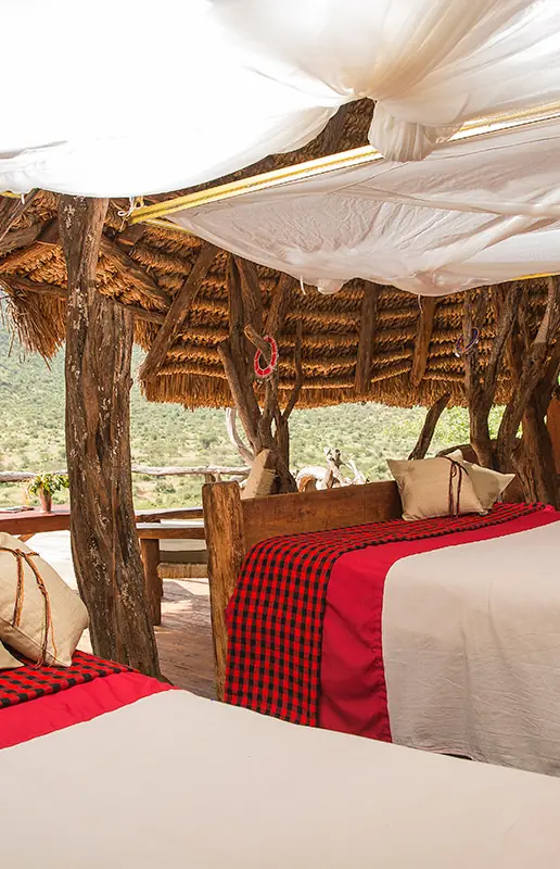 Safari lodge bedroom with red bedding and thatched roof, Il Ngwesi, Laikipia Highlands, Kenya