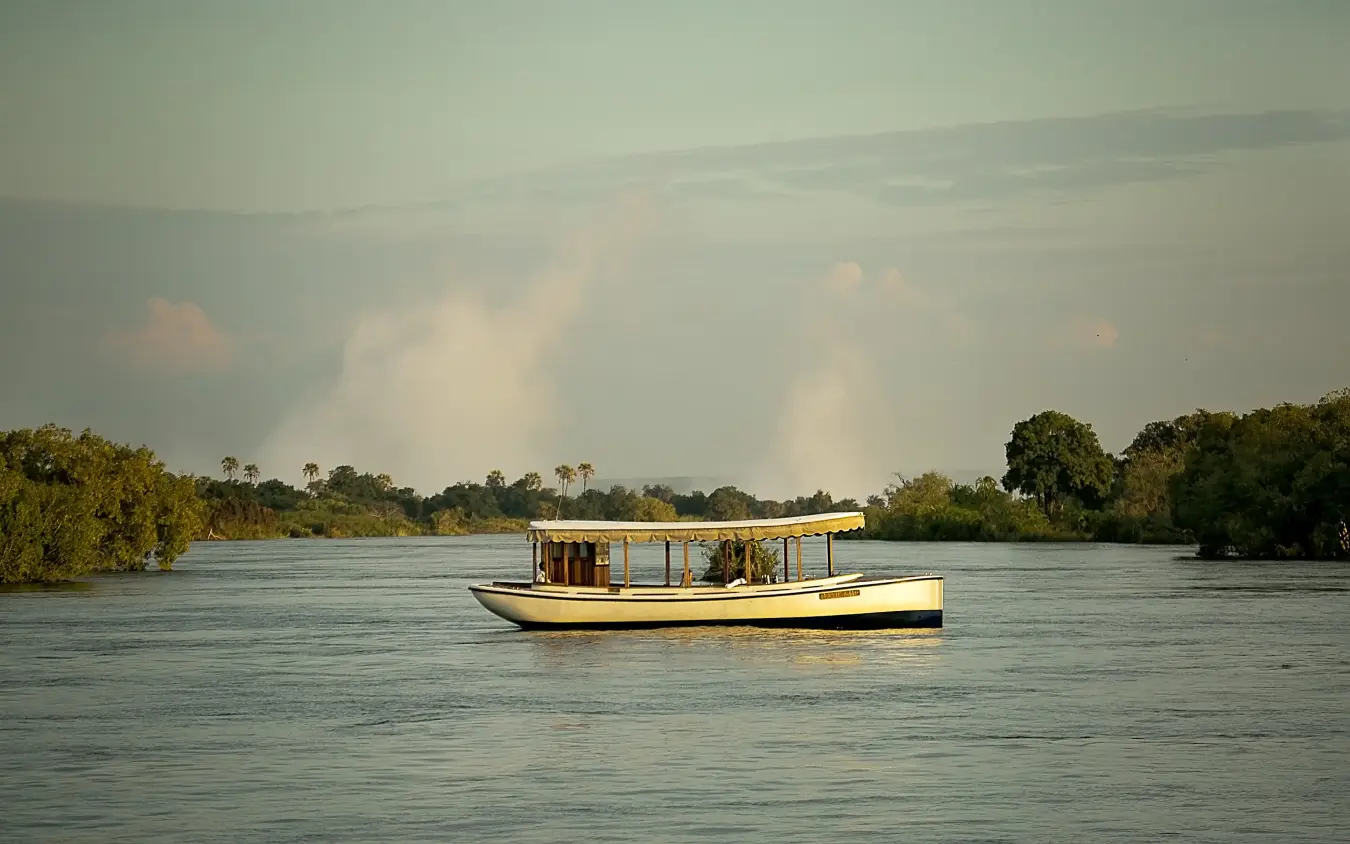 Traditional wooden boat moored in river with forested banks at dusk, Ilala Lodge Hotel, Victoria Falls, Zimbabwe