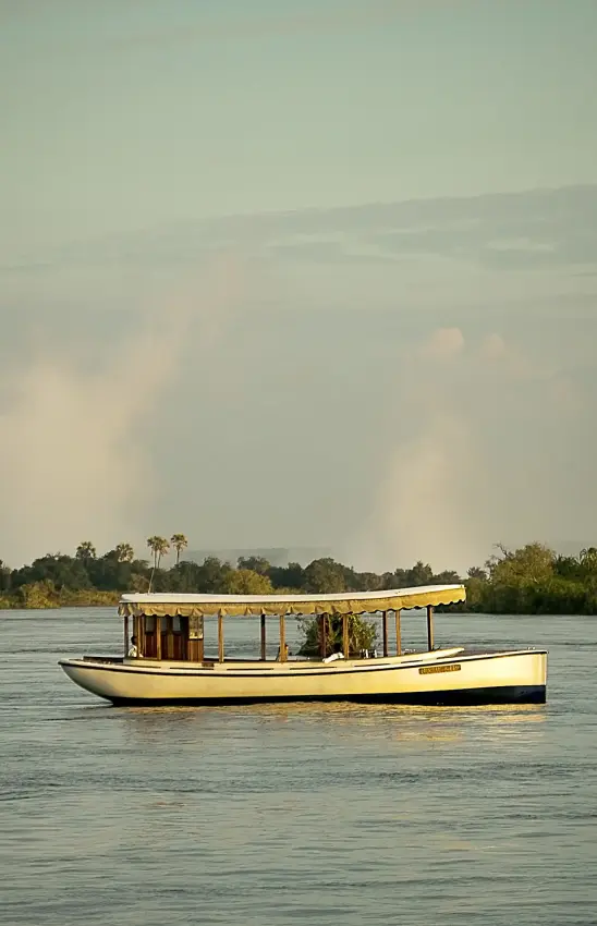 Yellow wooden boat on river with palm trees and clouds reflected in water, Ilala Lodge Hotel, Victoria Falls, Zimbabwe