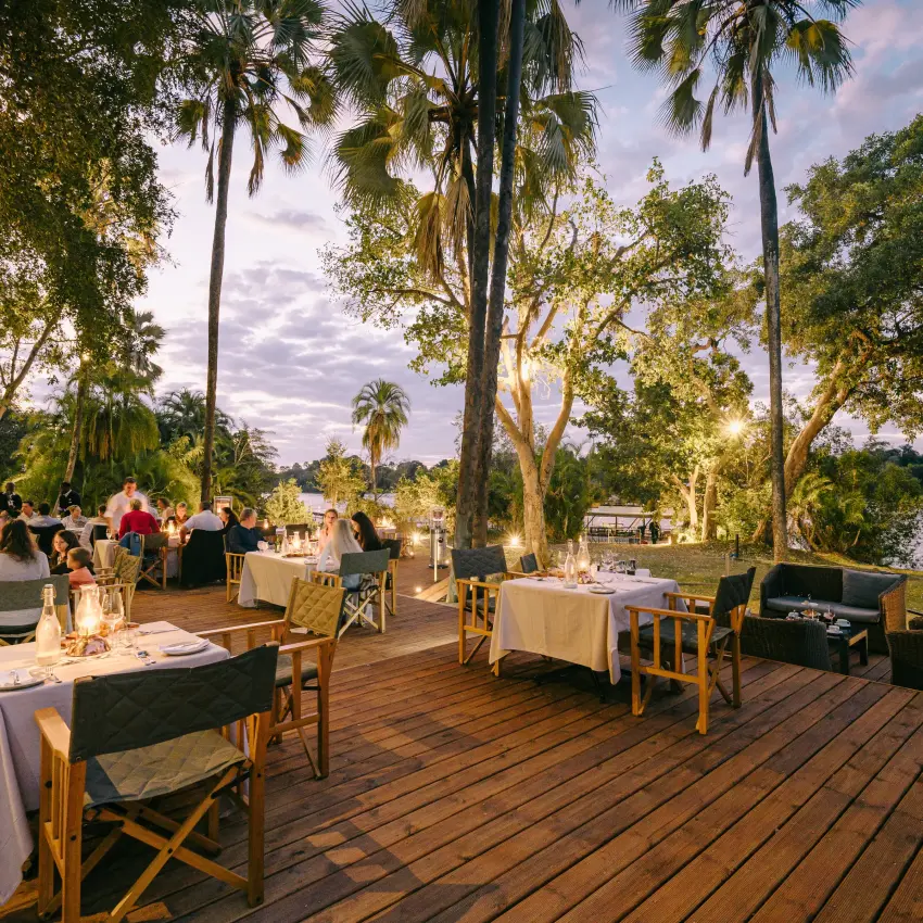 Outdoor dining deck with tables overlooking river at sunset, Ilala Lodge Hotel, Victoria Falls, Zimbabwe