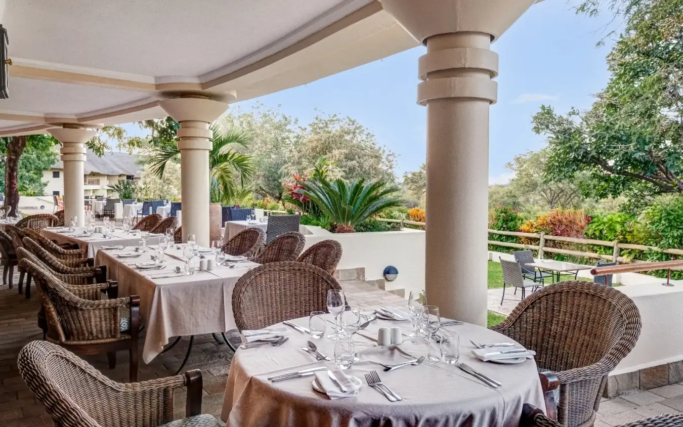 Outdoor dining pavilion with wicker chairs and formal table settings, Ilala Lodge Hotel, Victoria Falls, Zimbabwe
