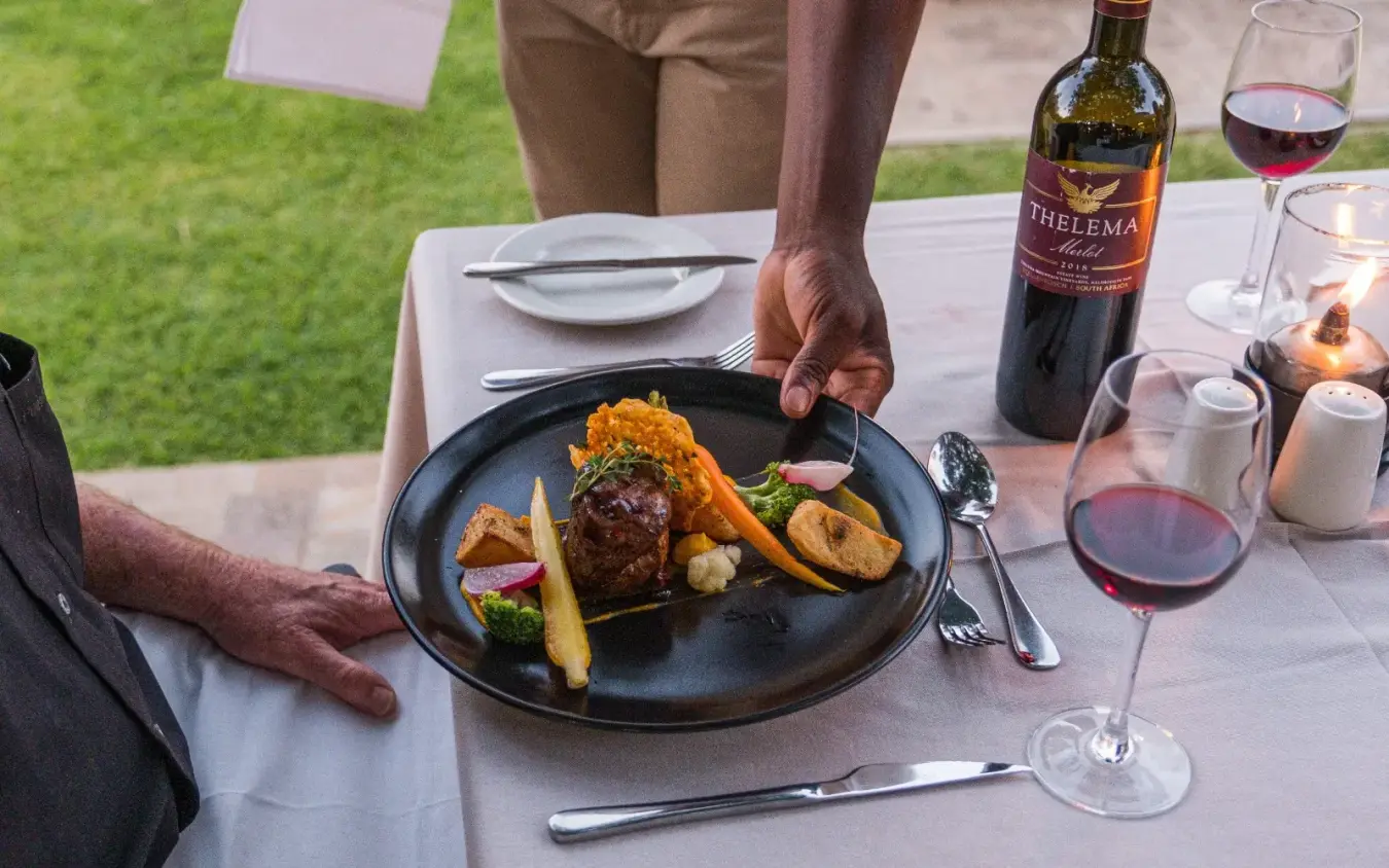 Outdoor dining table with plated meal and wine on manicured lawn, Ilala Lodge Hotel, Victoria Falls, Zimbabwe