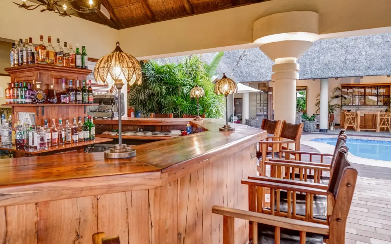 Luxury bar lounge with wooden counter overlooking swimming pool, Ilala Lodge Hotel, Victoria Falls, Zimbabwe