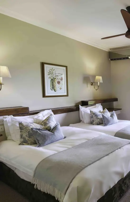 Twin beds with botanical cushions in light green bedroom with wall sconces, Ilala Lodge Hotel, Victoria Falls, Zimbabwe