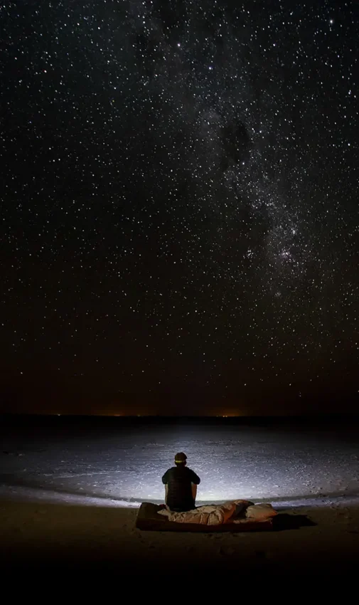 Person sitting alone under starry night sky, Makgadikgadi Pans, Botswana