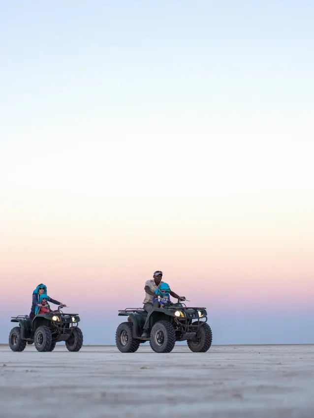 Three riders on quad bikes across vast salt pan at dusk, Jack’s Camp, Makgadikgadi Pans, Botswana