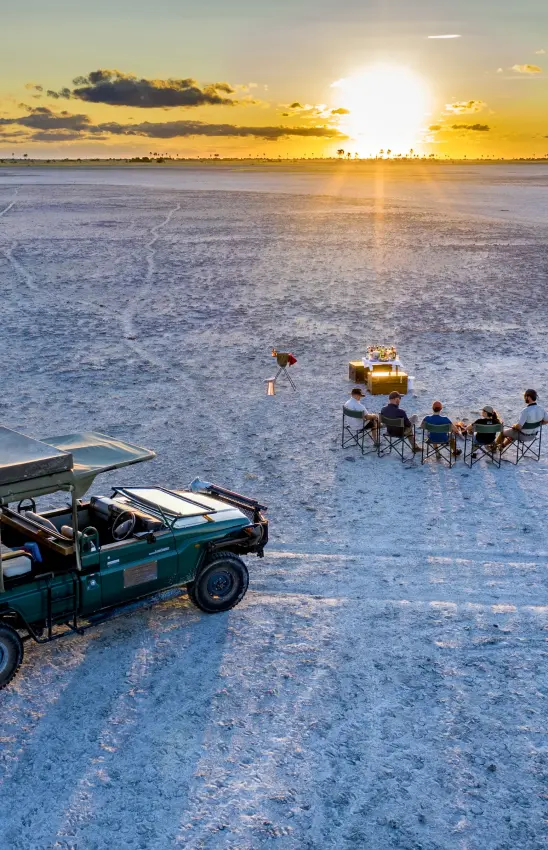 Vehicle and guests dining on salt pan at sunset, Makgadikgadi Pans, Botswana