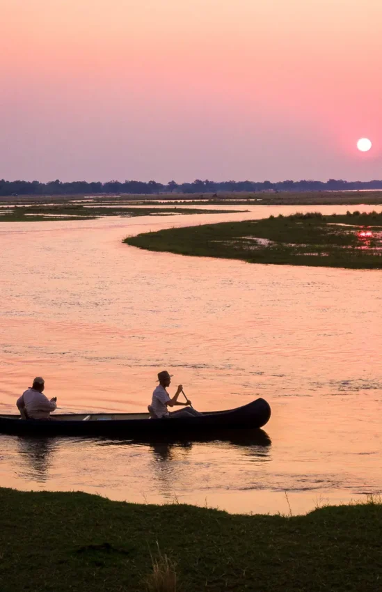 Two people paddling canoe at sunset on river, Mana Pools, Zimbabwe