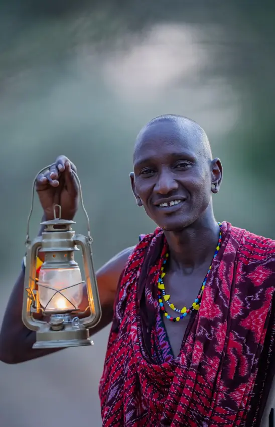 Man in red traditional clothing holding lantern smiling, Jongomero Camp, Ruaha National Park, Tanzania