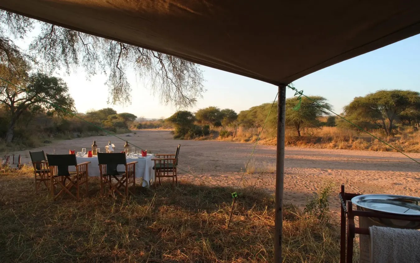 Outdoor dining setup under canvas canopy at sunset, Jongomero Camp, Ruaha National Park, Tanzania