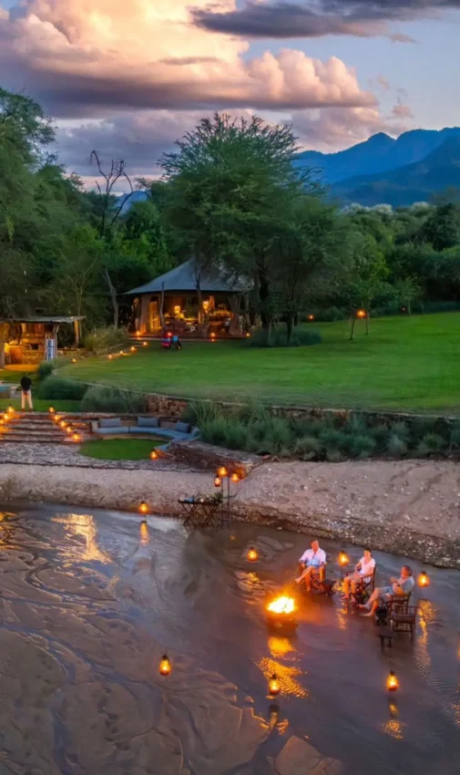 Riverside lodge at dusk with lit pathways and green lawn, Kalepo Camp, Northern Kenya, Kenya