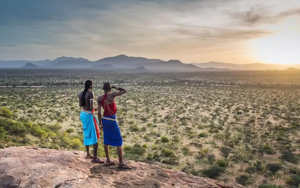 Two people viewing landscape from rocky outcrop at sunrise, Kalepo Camp, Northern Kenya, Kenya