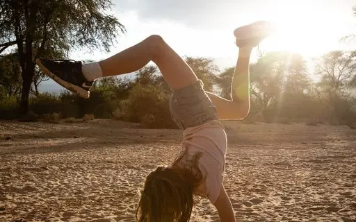 Guest doing handstand on sandy ground at sunset, Kalepo Camp, Northern Kenya, Kenya