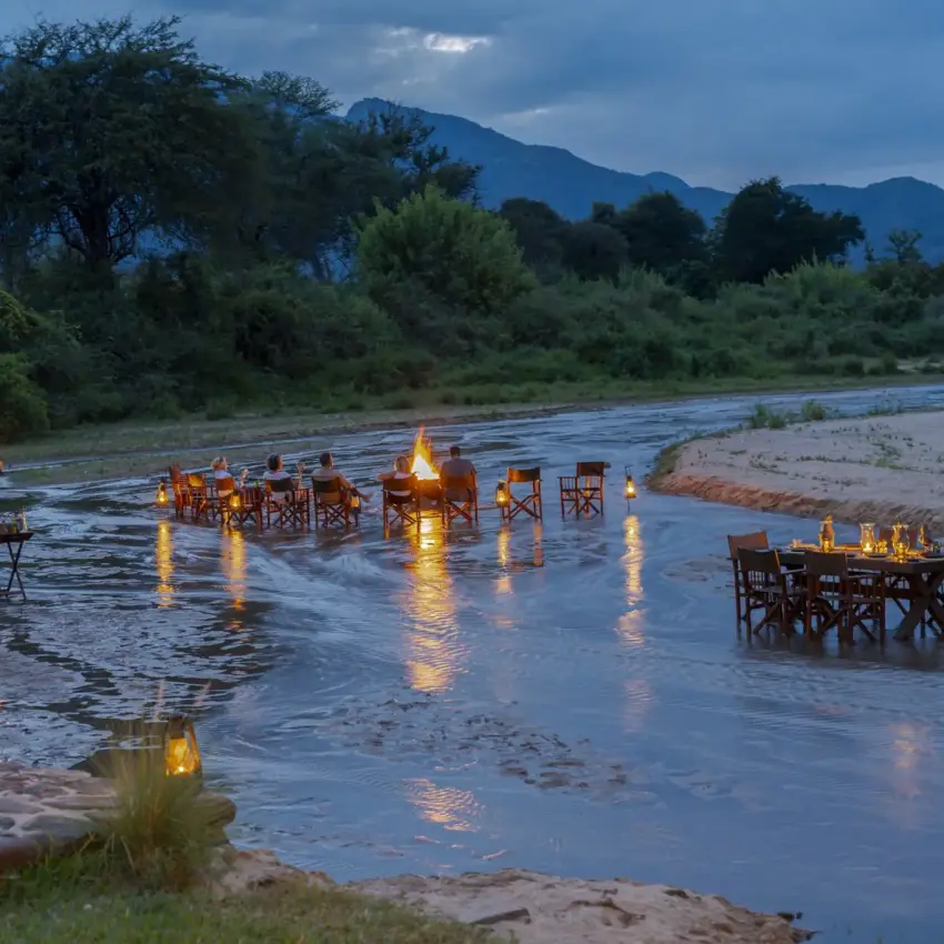 Candlelit dining tables set in shallow river at dusk, Kalepo Camp, Northern Kenya, Kenya