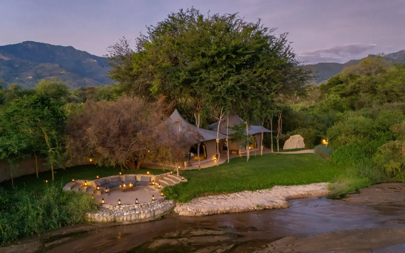 Riverside lodge with illuminated fire pit and mountain backdrop, Kalepo Camp, Northern Kenya, Kenya