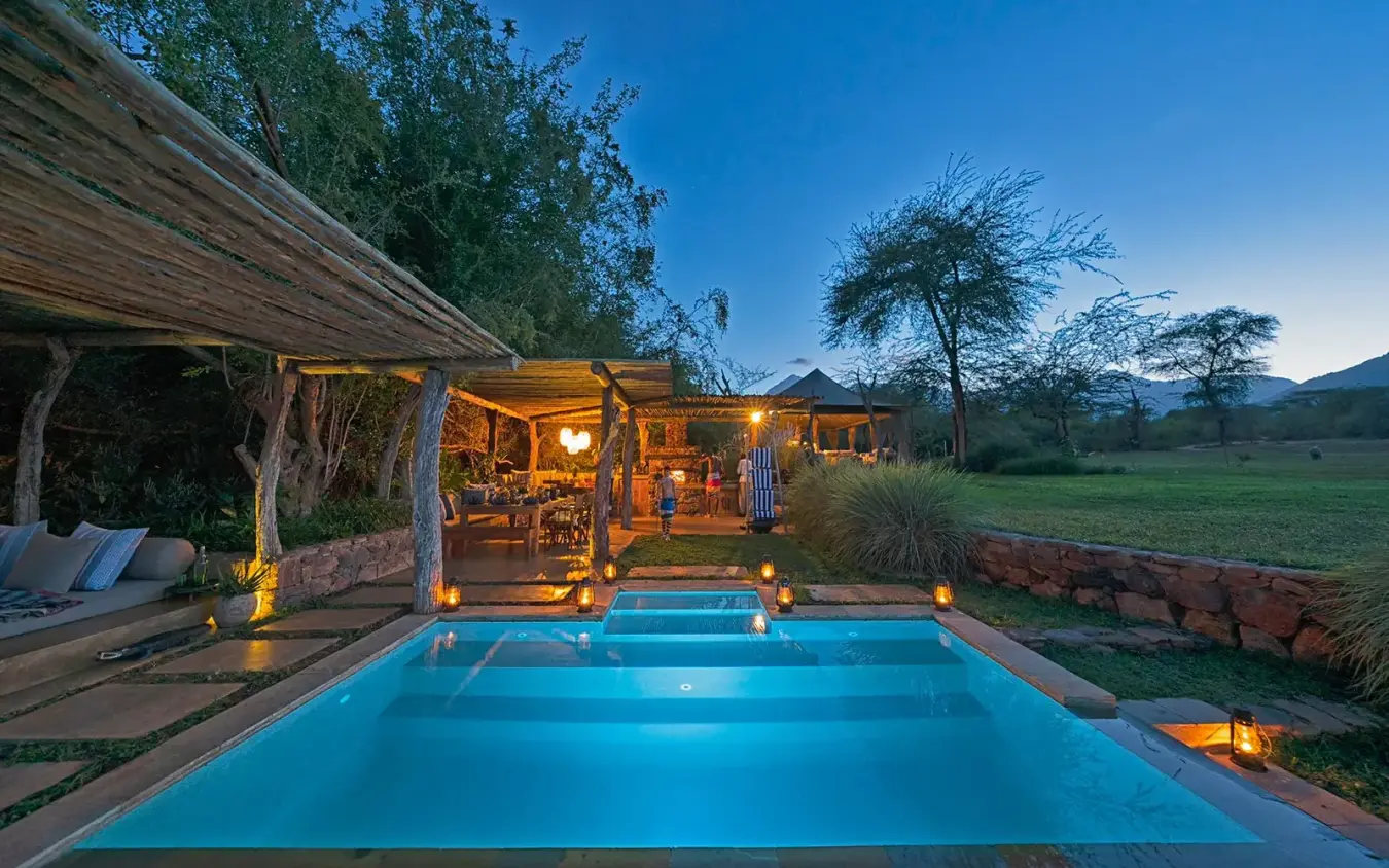 Illuminated swimming pool with lodge buildings at dusk, Kalepo Camp, Northern Kenya, Kenya