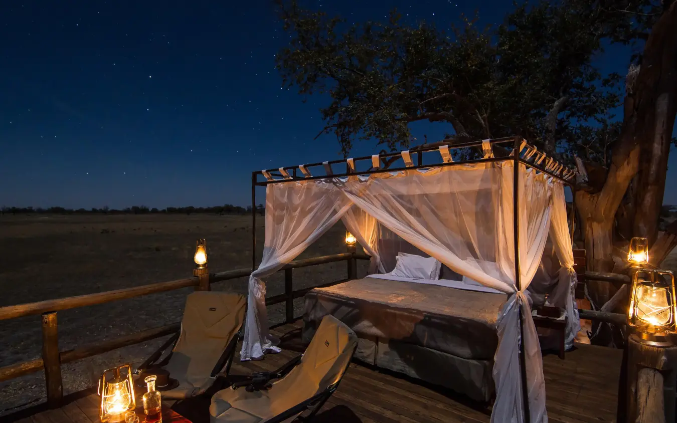 Outdoor bedroom pavilion with curtains overlooking savanna at night, Kanana, The Okavango Delta, Botswana